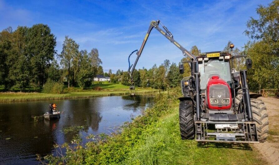 Työkone vesistön rannalla ruoppaamassa vesistöä.