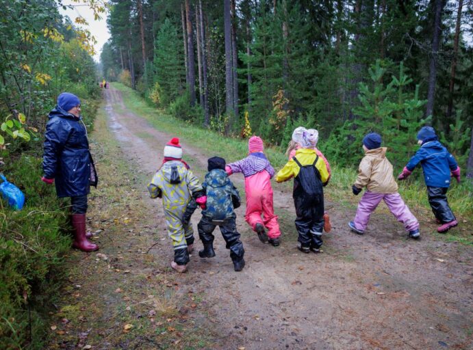 Metsäinen tie, jossa lapset lähdössä juoksukilpaan sadeasut päällä.