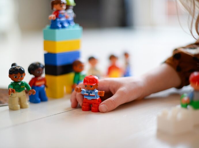 Lapsen kädessä legoukkeli, taustalla muita legoja.