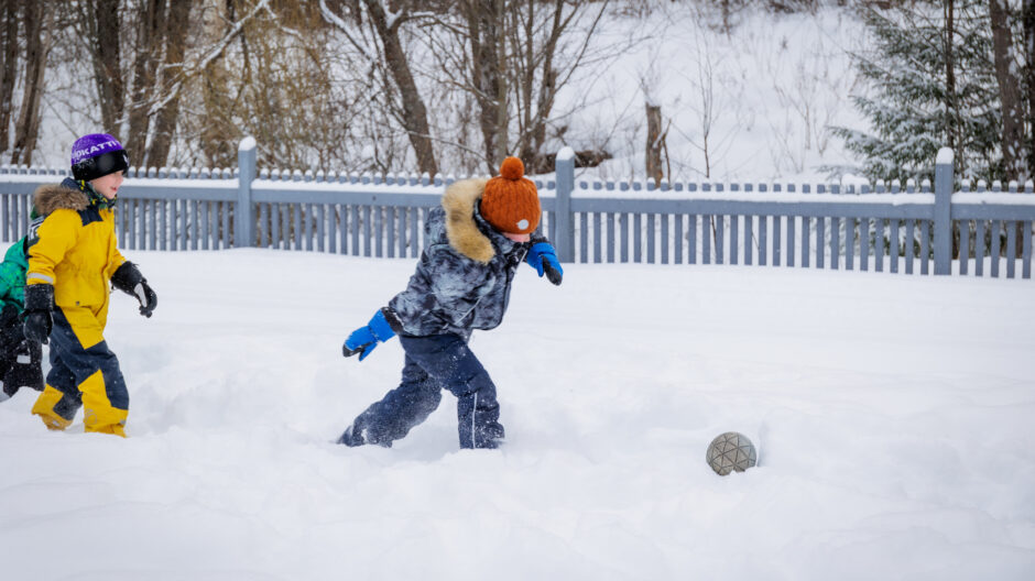 Lapset leikkivät jalkapalloa lumessa.