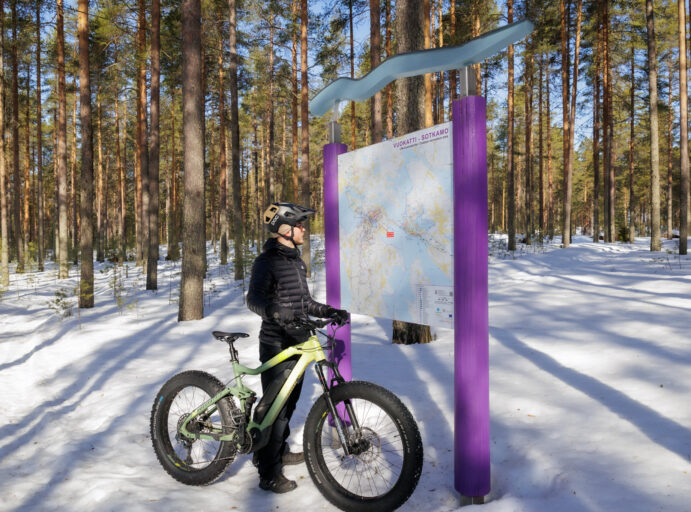 Maastopyöräilijä talvella katsomassa Vuokatin ja Sotkamon alueen reittejä ulkokartasta.