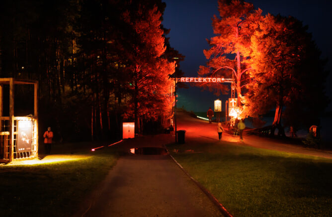 Valotaidefestifaalin sisäänkäynti Hiukan harjuilla, jossa upeat männyt loistavat punaisena.