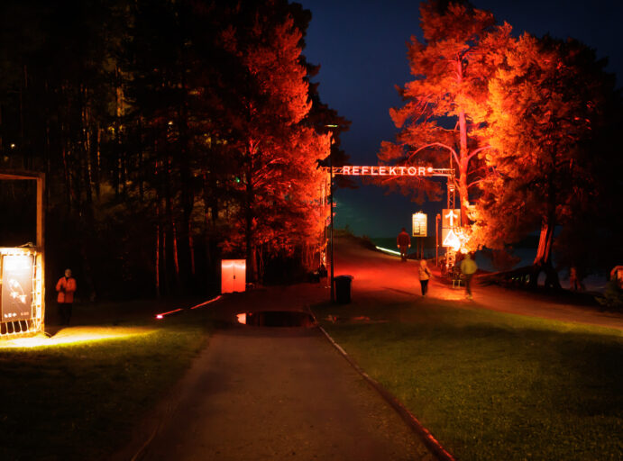 Valotaidefestifaalin sisäänkäynti Hiukan harjuilla, jossa upeat männyt loistavat punaisena.