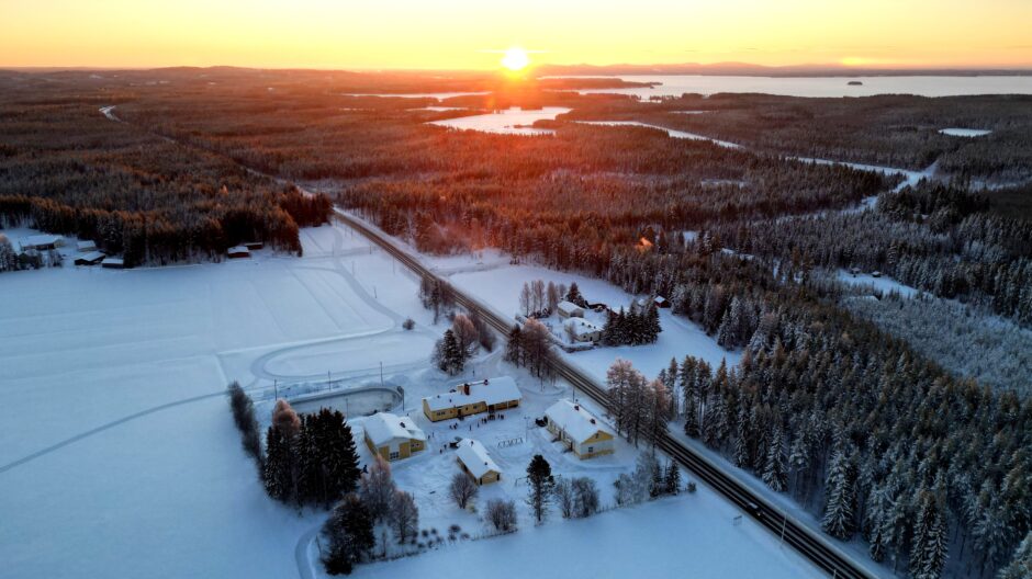 Pohjavaaran koulun alueelta otettu ilmakuva, jossa aurinko laskee taivaanrantaan.