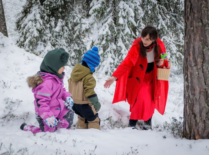 Punaisiin pukeutunut "Punahilkka" ja kaksi lasta talvisessa metsässä.