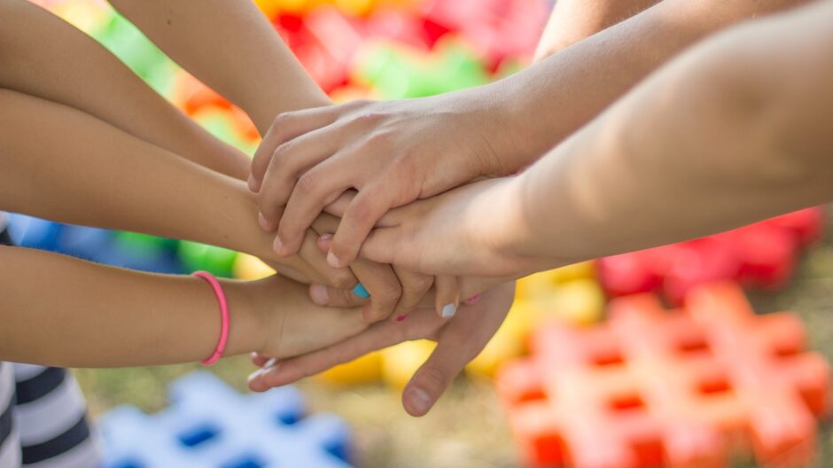 Kädet yhdessä päällekkäin, taustalla värikkäitä leikkipalikoita.