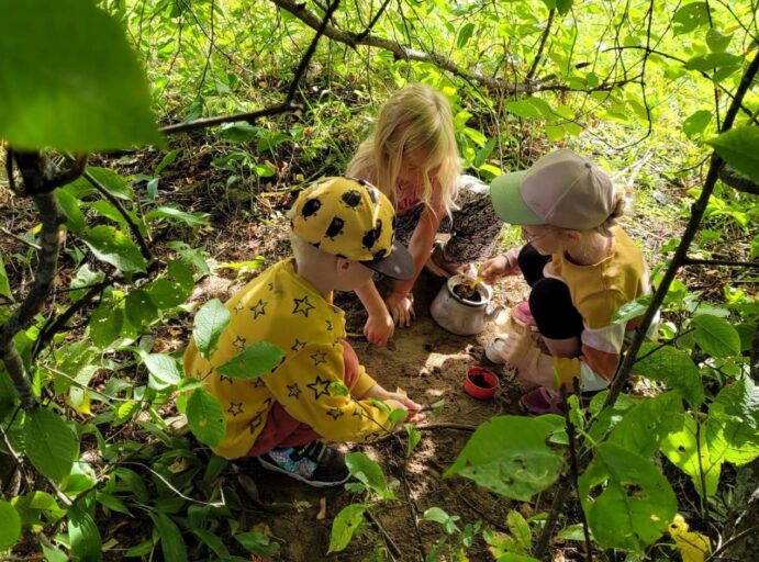 Kolme lasta puunlehtien suojassa "majassa" omissa leikeissään.