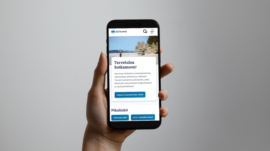 Käsi pitelee mobiilia, jossa näkyvät Sotkamon kunnan uudet verkkosivut.