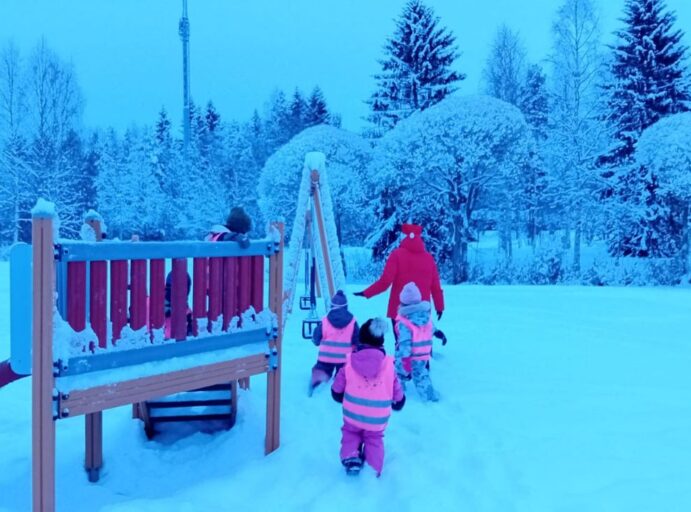 Iltahämyinen leikkipuisto, jossa lapsia liukumäessä ja yksi tonttupukuinen aikuinen.